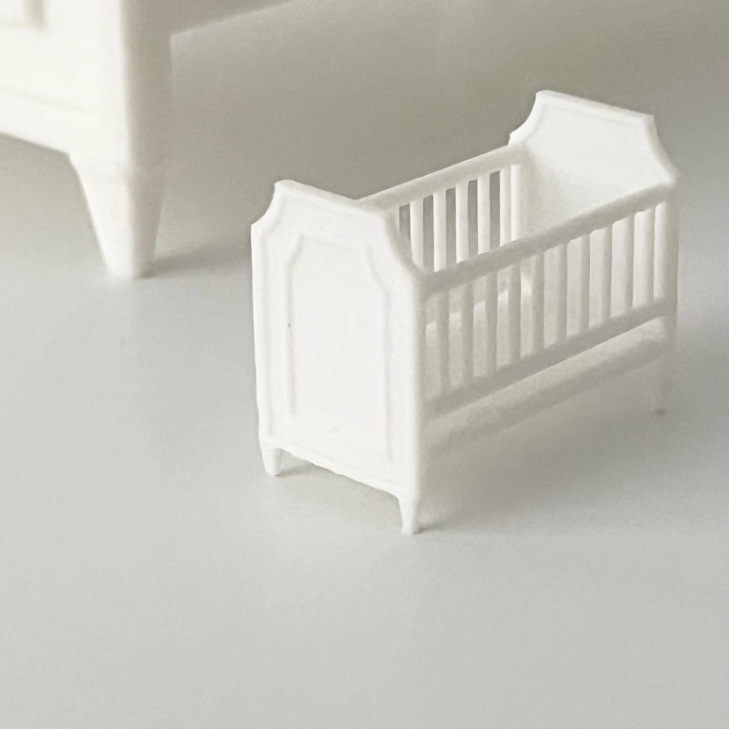 White baby crib in 1:48 scale on a light gray background