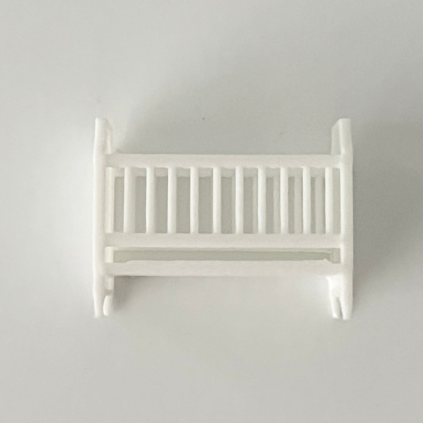 Side view of White baby crib in 1:48 scale on a light gray background